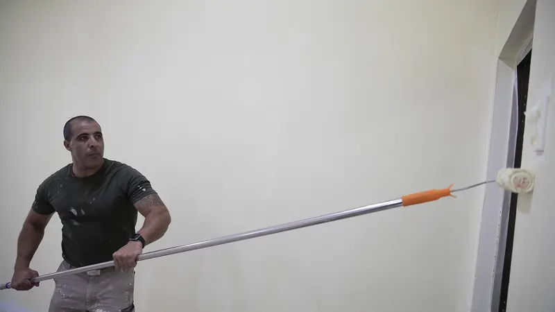 Maler mit Farbroller an einer Wand in einem Innenraum
